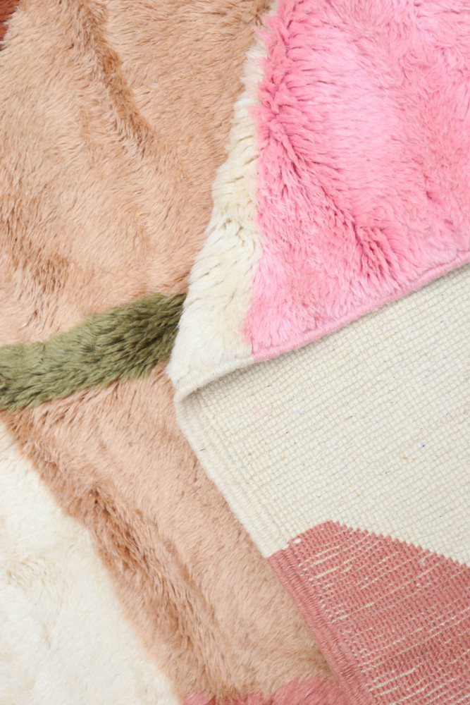 Tapis berbère coloré avec des motifs géométriques, dominé par le rose, le beige et le vert, offrant une texture douce.