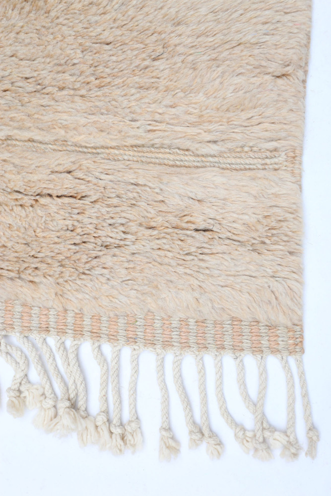 Tapis berbère en laine beige avec des franges, au design minimaliste et texture douce.