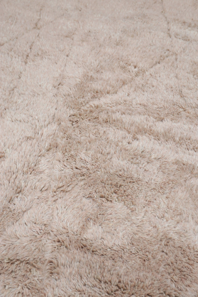 Tapis berbère doux en beige, au style minimaliste avec des motifs géométriques subtils et une texture pelucheuse.