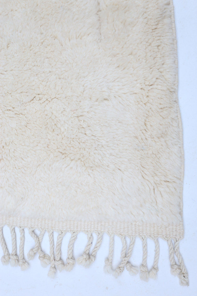 Tapis berbère en laine blanche, au style minimaliste, avec des motifs doux et des franges délicates.