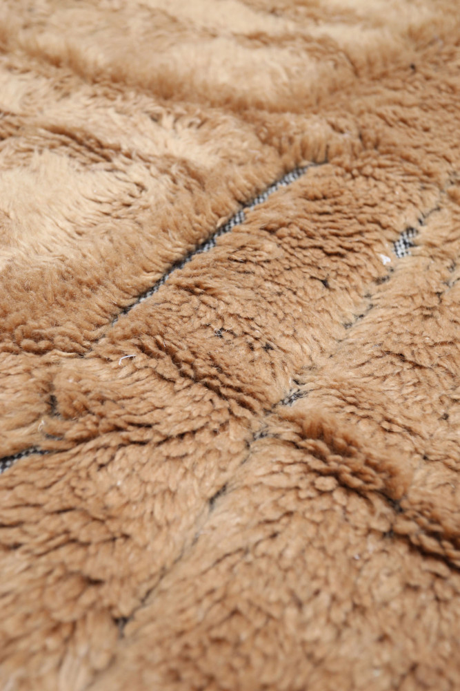Tapis berbère en laine beige avec des motifs géométriques en noir, offrant une texture douce et chaleureuse.