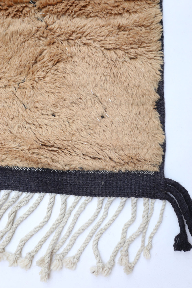 Tapis berbère en laine beige avec motifs géométriques et franges noires, apportant une touche chaleureuse et authentique.