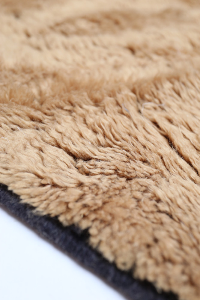 Tapis berbère en fausse fourrure beige avec des motifs doux et un contour noir élégant, parfait pour un intérieur chaleureux.