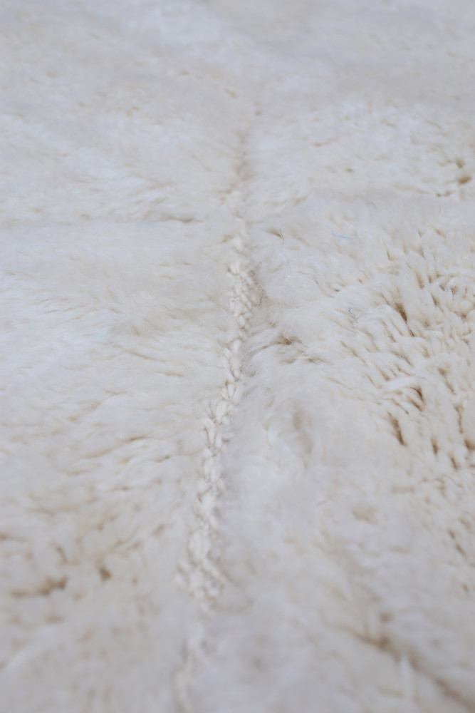 Tapis berbère douillet, en laine blanche, avec des motifs texturés et un design minimaliste.