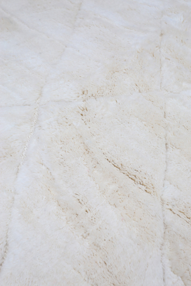 Tapis berbère en laine, couleur beige clair avec des motifs géométriques subtils et une texture douce et moderne.