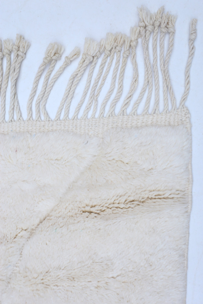 Tapis berbère en laine naturelle, couleur crème, avec des motifs tissés délicats et des franges.
