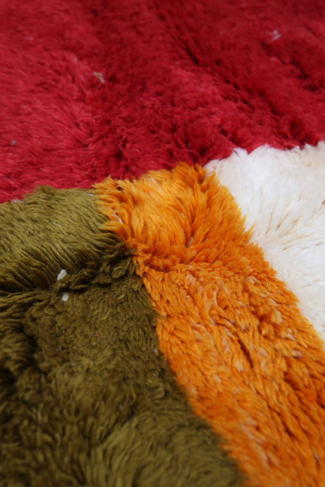 Tapis berbère coloré avec des motifs géométriques en rouge, orange, vert et blanc, apportant une touche chaleureuse et authentiq