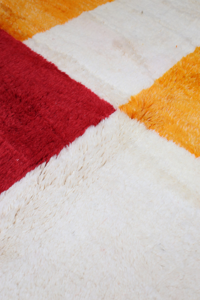 Tapis berbère coloré avec des motifs géométriques en rouge, orange et blanc, apportant une touche artisanale à votre intérieur.