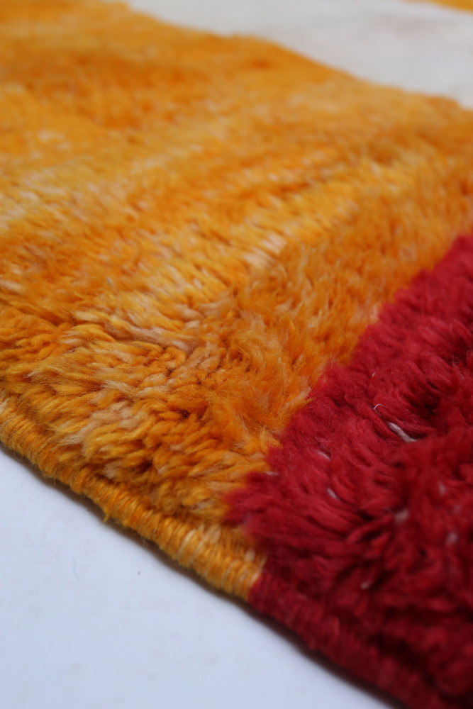 Tapis berbère aux couleurs vives avec des dégradés d\'orange et des touches de rouge, affichant un design moderne et stylisé.
