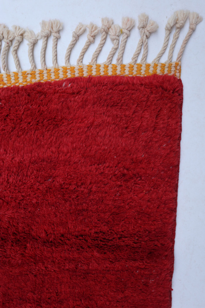 Tapis berbère rouge aux motifs simples avec des franges, apportant une touche chaleureuse et artisanale à votre intérieur.