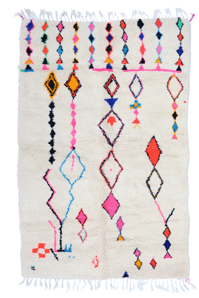 Tapis berbère à motifs géométriques colorés, dominé par du blanc, avec des touches de rose, bleu, noir et orange.