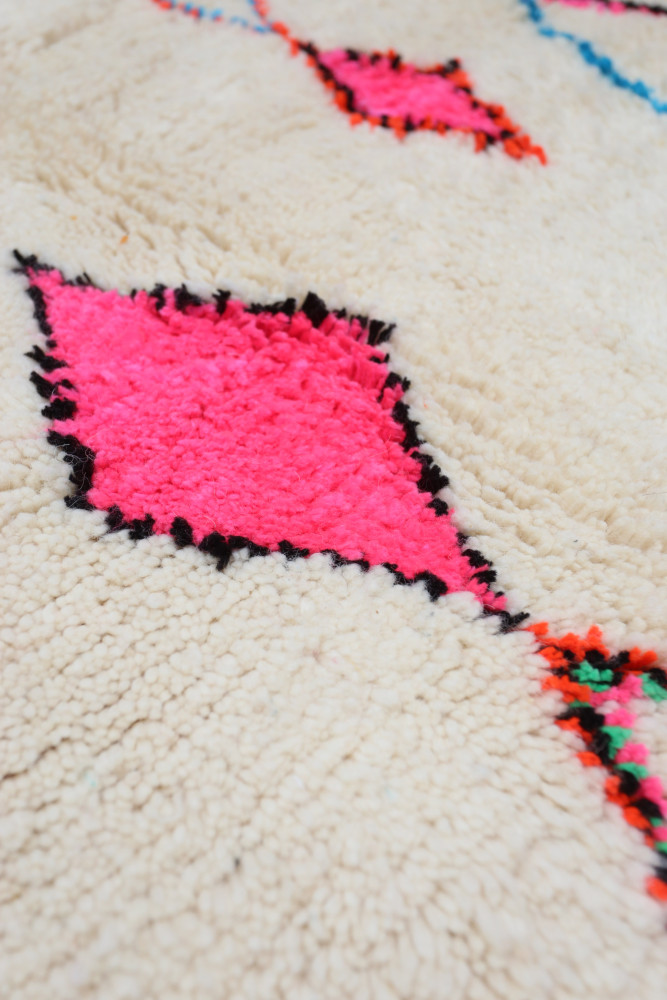 Tapis berbère au fond crème avec motifs géométriques en rose fluo et accent noir, ajoutant une touche vibrante et artisanale.