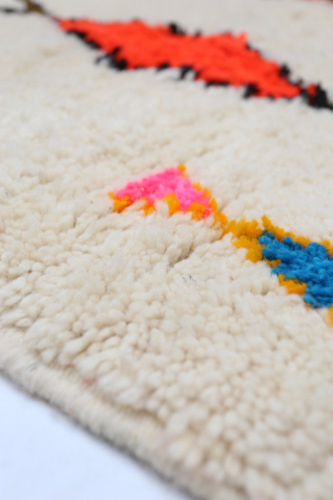 Tapis berbère aux motifs colorés avec des touches de rouge, rose, bleu sur fond crème, ajoutant une touche moderne et chaleureus