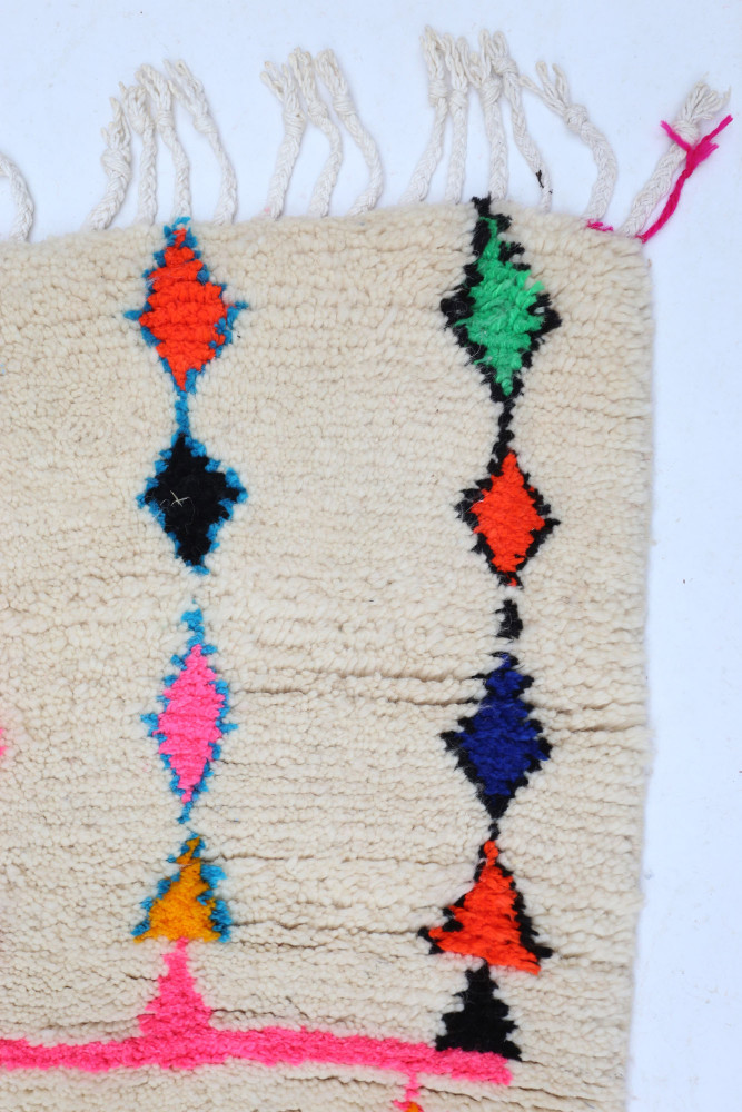 Tapis berbère en laine avec motifs géométriques colorés, dominés par le beige, le noir, le rose et le bleu.