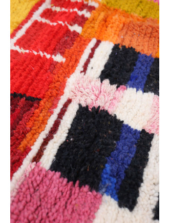 Tapis berb&egrave;re color&eacute; avec des motifs g&eacute;om&eacute;triques et des teintes vives de rouge, rose, noir et bleu.