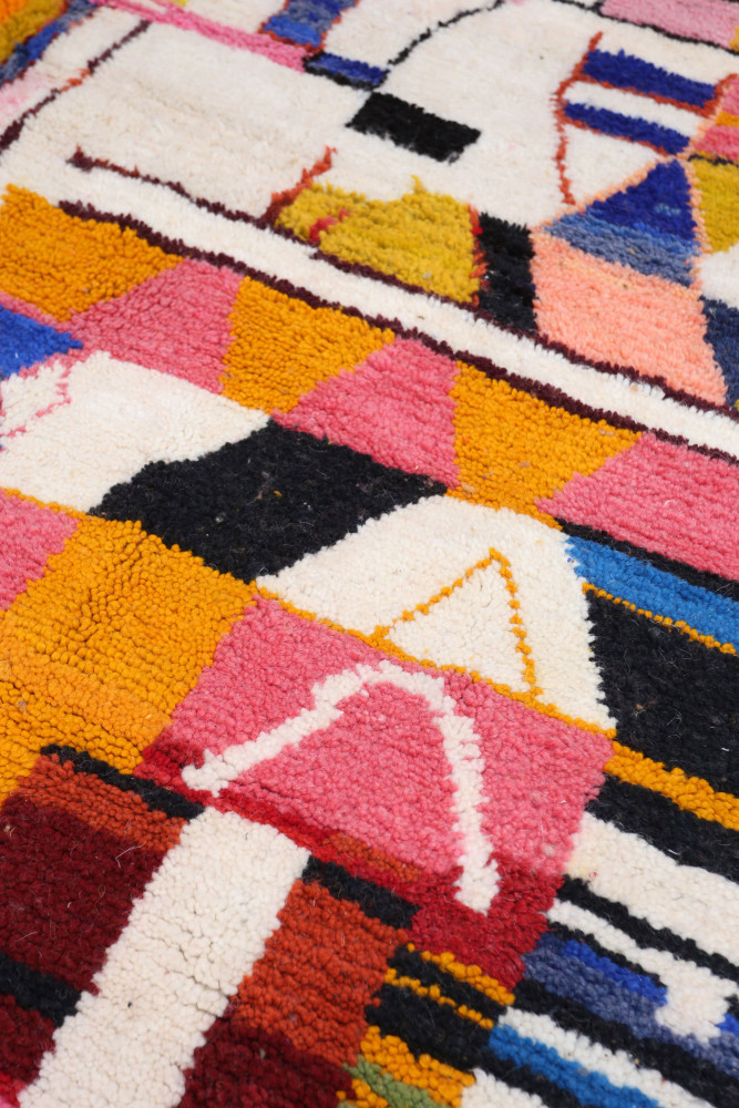 Tapis berbère aux motifs géométriques colorés avec des teintes vives de rose, jaune, bleu et noir, parfait pour décorer.
