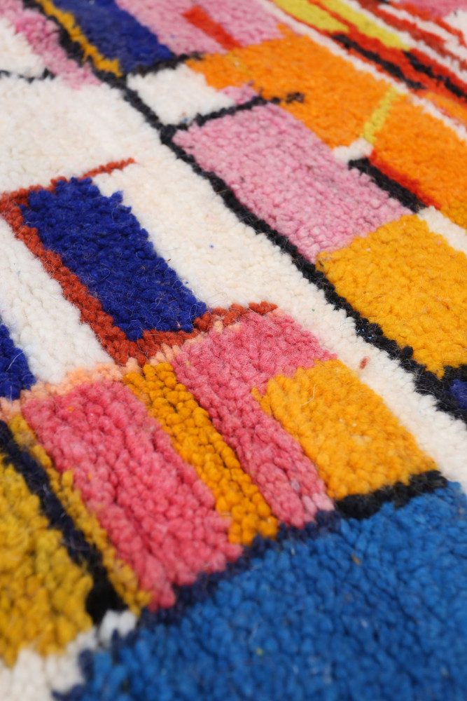 Tapis berbère coloré avec des motifs géométriques en rose, bleu, jaune et orange sur fond crème.