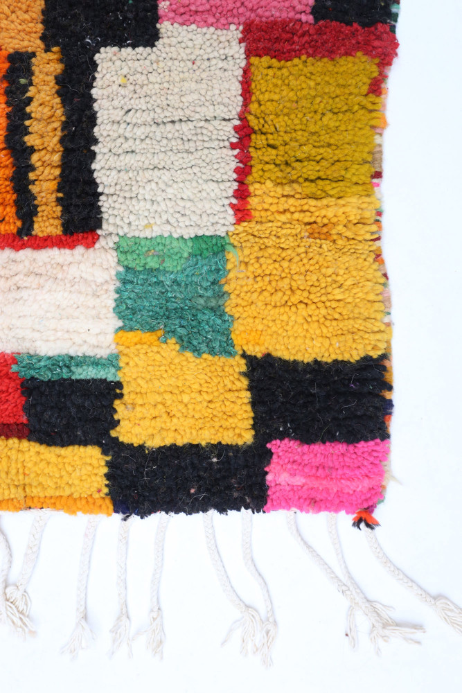 Tapis berbère coloré avec des motifs géométriques en jaune, rose, noir et vert, apportant une touche contemporaine.