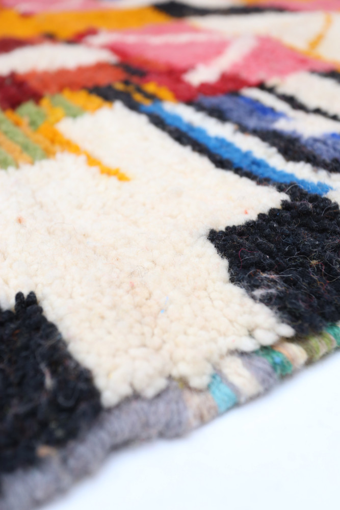 Tapis berbère coloré avec un design géométrique vibrant, dominant les teintes blanches, noires et multicolores.