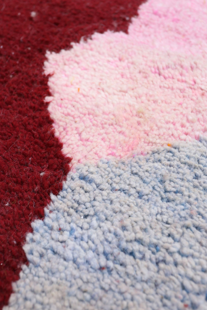 Tapis berbère aux motifs géométriques avec des nuances de rouge, rose et bleu, offrant une esthétique moderne et colorée.
