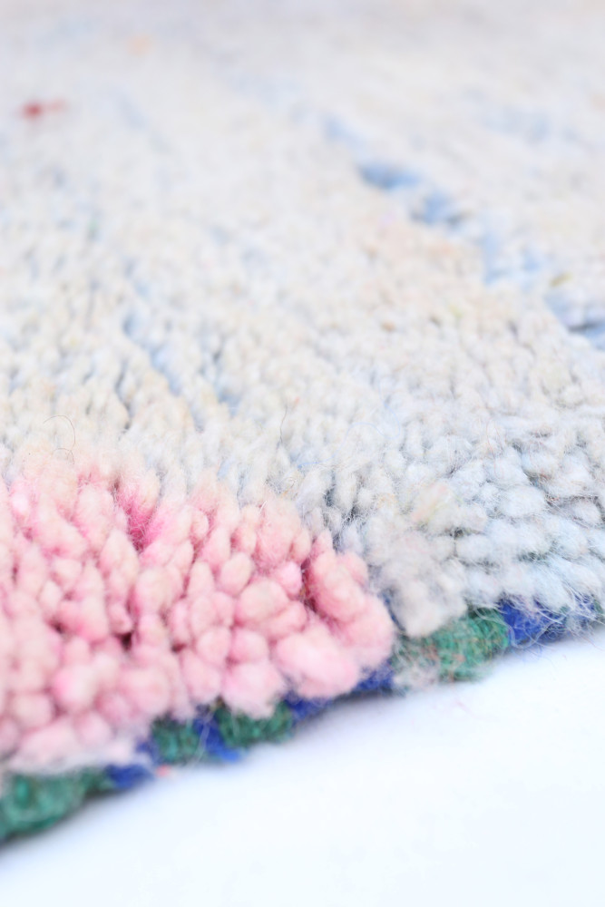 Tapis berbère en laine avec des nuances de bleu, rose et vert, ornés de motifs géométriques traditionnels.
