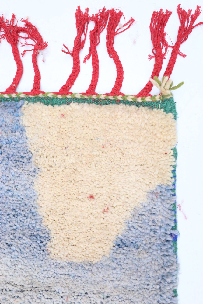 Tapis berbère aux motifs géométriques, dominé par des teintes bleu et beige avec des touches de rouge et de vert.