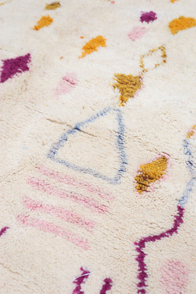 Tapis berbère aux motifs géométriques en rose, bleu et jaune sur fond crème offrant une touche moderne et ethnique.