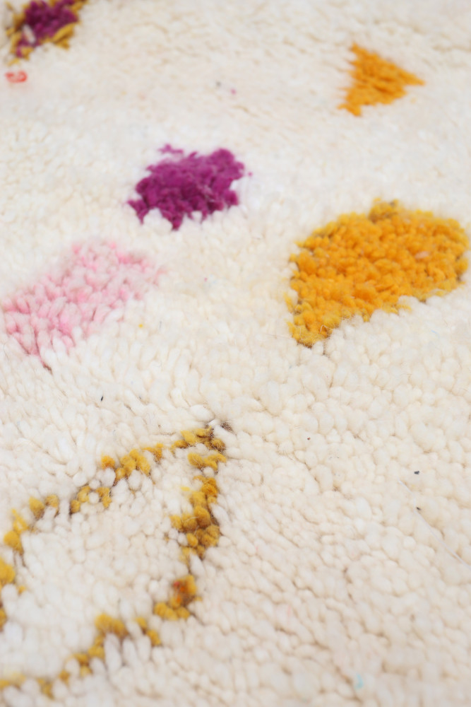 Tapis berbère en laine crémeux avec des motifs géométriques colorés en rose, violet et jaune.