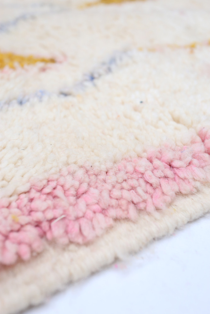 Tapis berbère à motif géométrique, couleurs beige et rose pastel avec des touches de jaune et texture douce en laine.