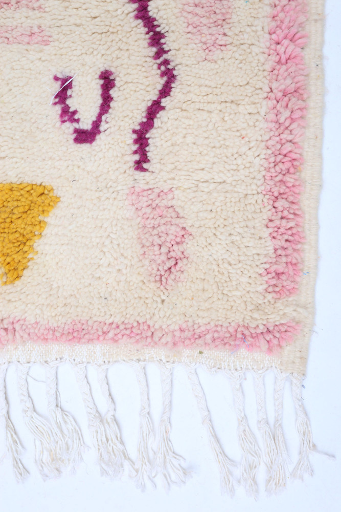 Tapis berbère aux motifs géométriques en rose, jaune et violet sur fond crème, ajoutant une touche artistique et chaleureuse.