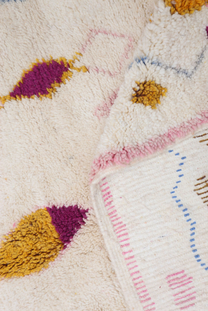 Tapis berbère aux motifs colorés en rose, violet et jaune sur fond crème, offrant une touche artisanale et chaleureuse.