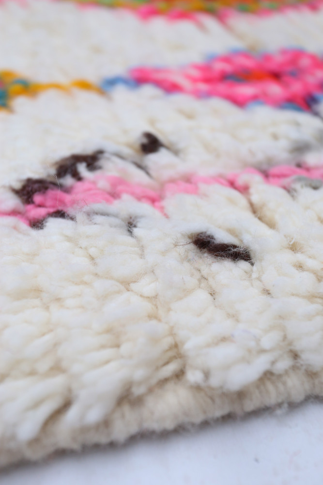 Tapis berbère aux couleurs vives avec motifs géométriques sur fond crème, ajoutant une touche artisanale à votre intérieur.