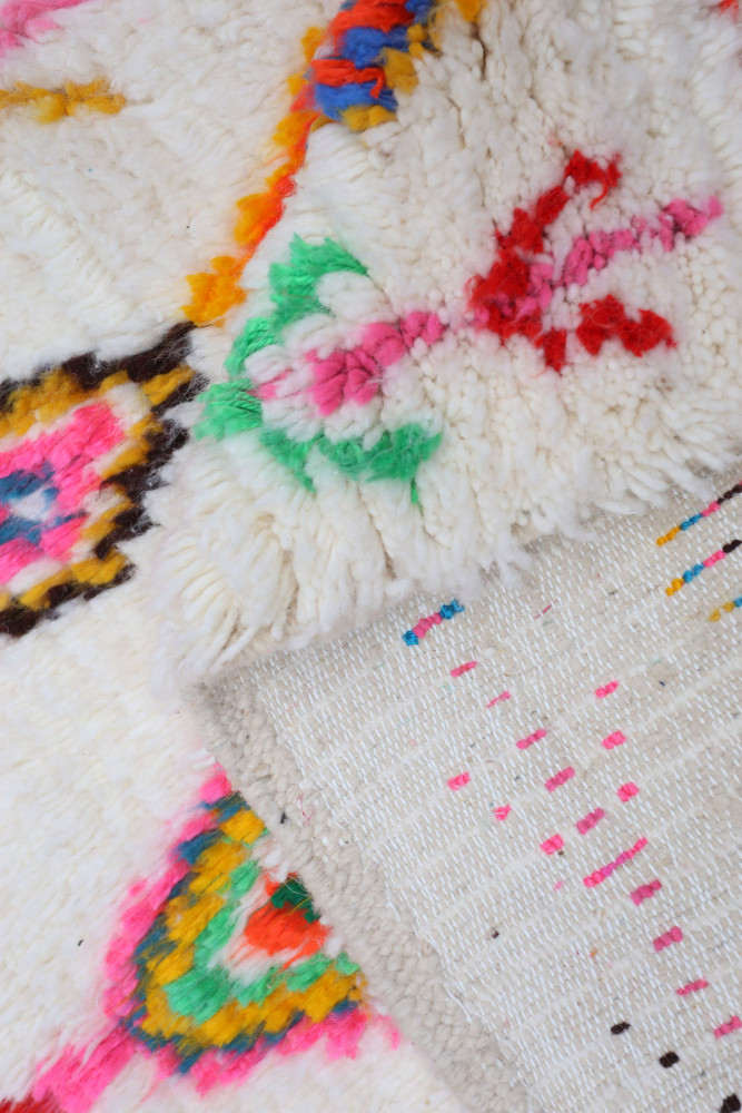 Tapis berbère aux motifs colorés, mélanges de couleurs vives comme le rose, vert et jaune sur fond blanc.