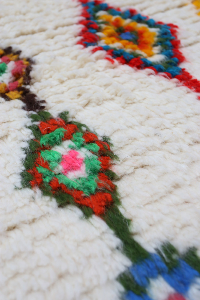 Tapis berbère coloré aux motifs géométriques avec des teintes vives de rouge, vert, bleu et jaune sur fond crème.