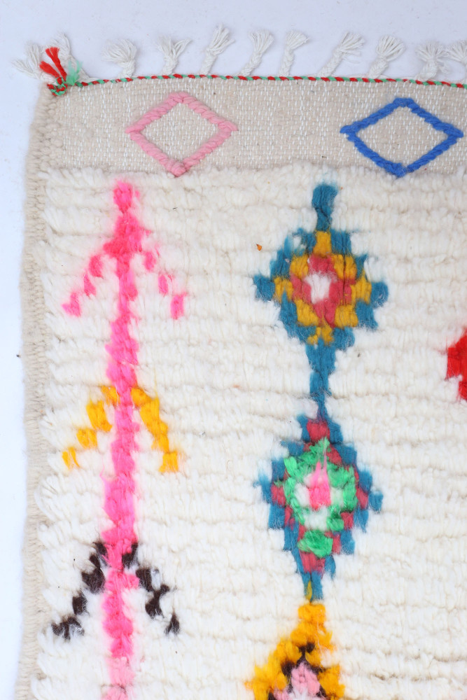 Tapis berbère en laine beige avec des motifs géométriques colorés en rose, bleu, vert et jaune.