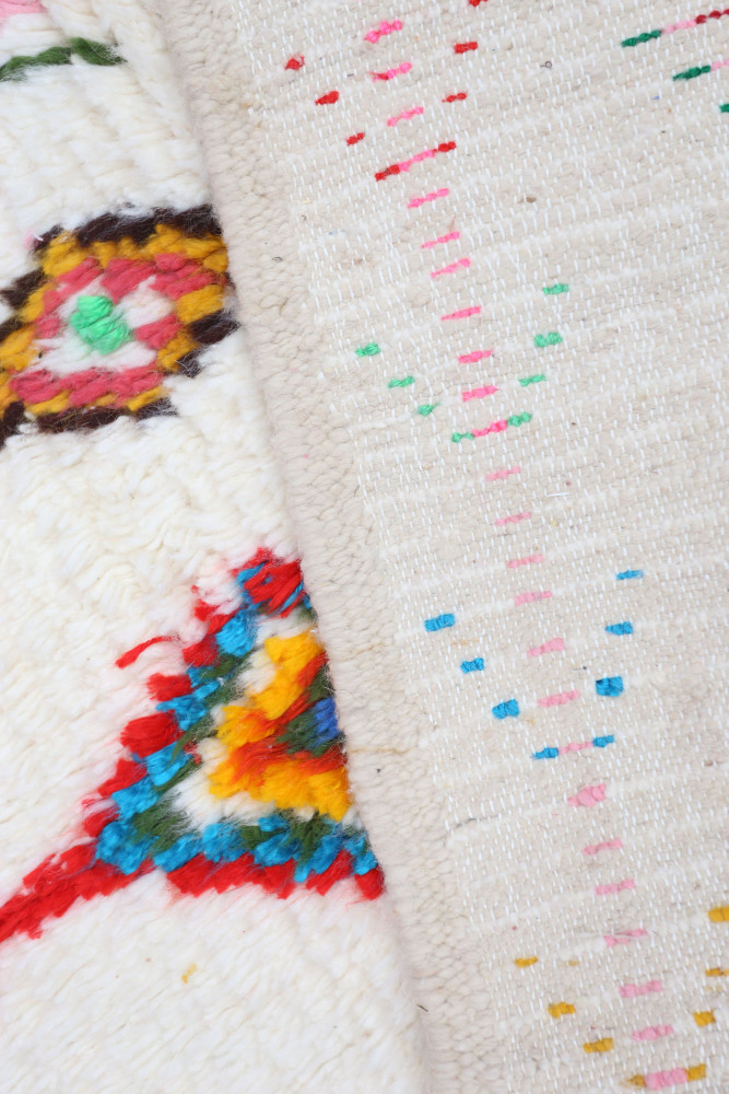 Tapis berbère aux motifs colorés sur fond crème, présentant des couleurs vives comme le rouge, le bleu et le jaune.