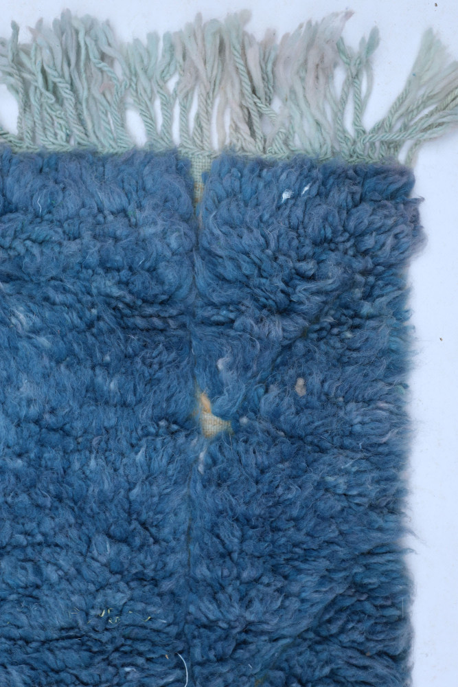 Tapis berbère en laine bleue avec des motifs texturés et franges délicates, ajoutant une touche artisanale à votre décoration.