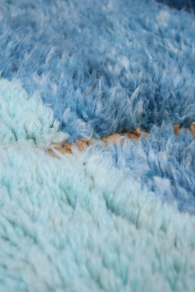 Tapis berbère aux teintes bleues et turquoise avec des motifs abstraits et un aspect pelucheux.