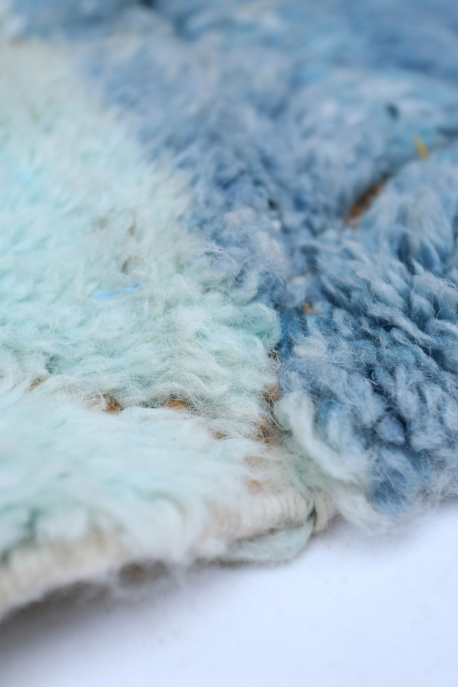 Tapis berbère bleu et vert, avec des motifs doux et une texture laineuse, idéal pour une décoration moderne.