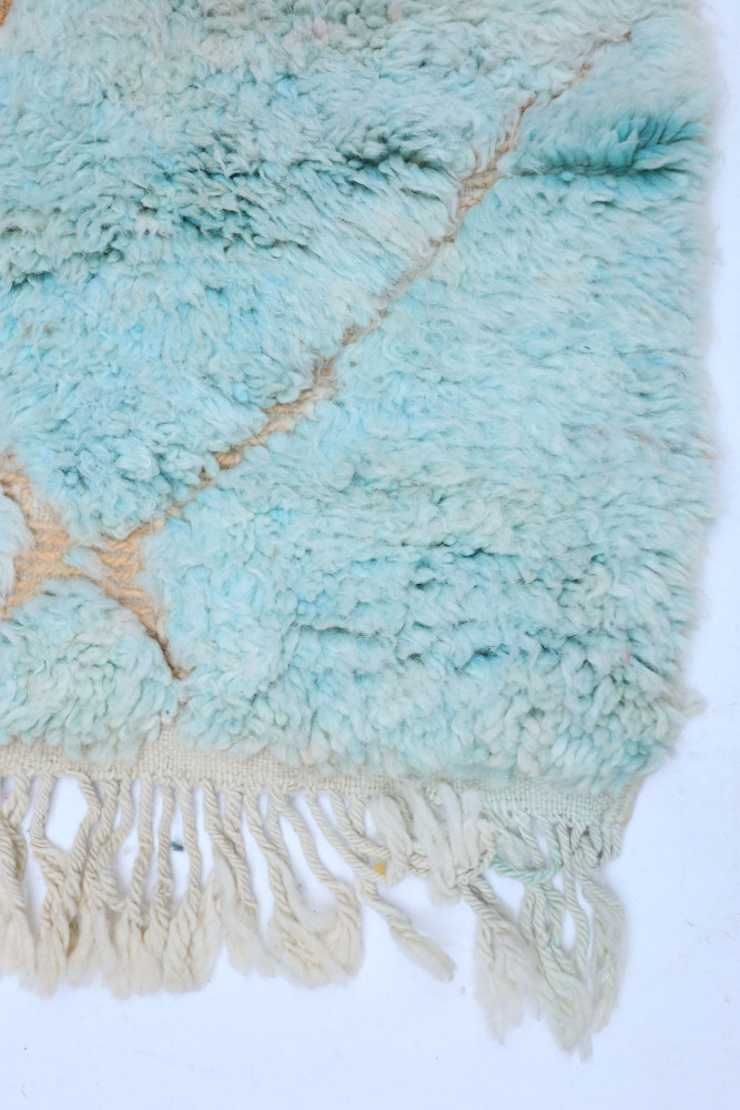 Tapis berbère en laine, bleu clair avec motifs géométriques, textures moelleuses et franges délicates.