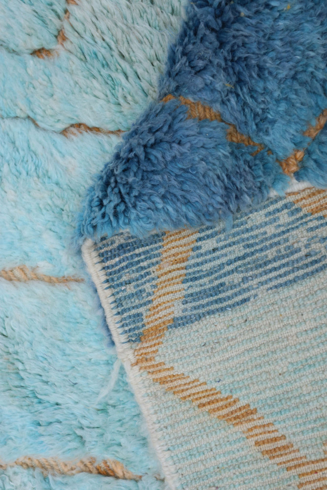 Tapis berbère en bleu vif et crème, avec des motifs géométriques et des textures douces et luxuriantes.