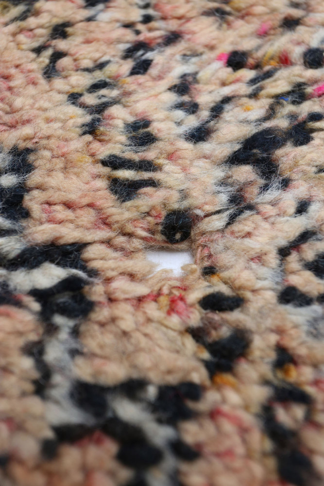 Tapis berbère aux motifs géométriques, couleurs beiges, noirs et touches de rose, apportant chaleur et style ethnique.
