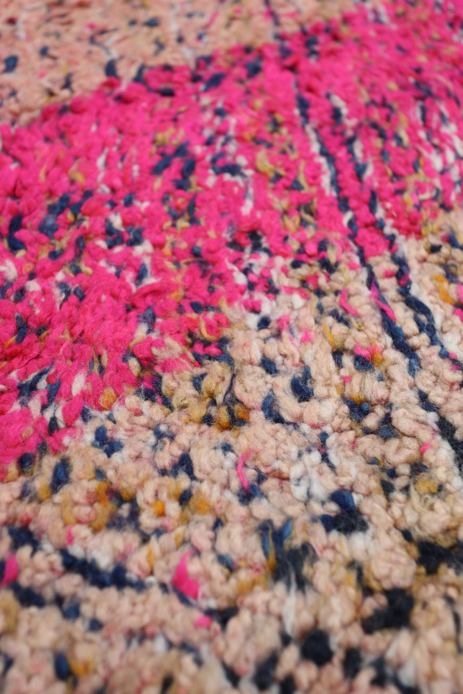 Tapis berbère coloré avec des motifs géométriques en rose, beige et bleu marine, offrant une touche moderne et artisanale.