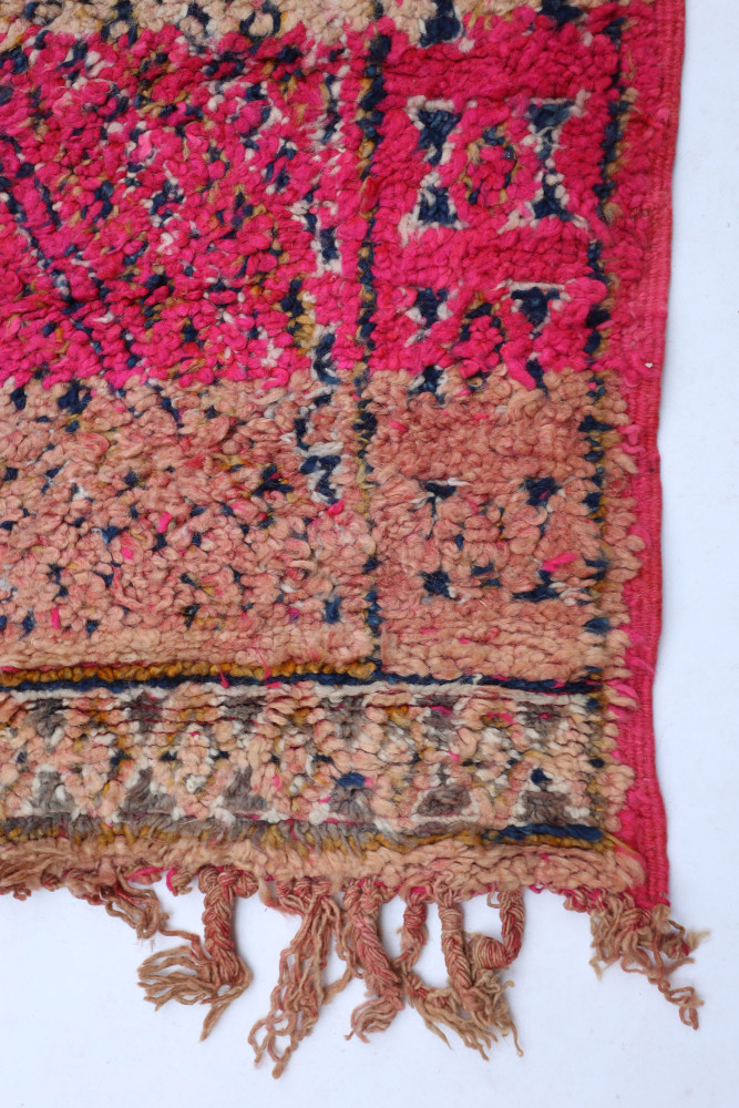 Tapis berbère coloré aux motifs géométriques, dominé par des tons rose, beige et bleu marine.