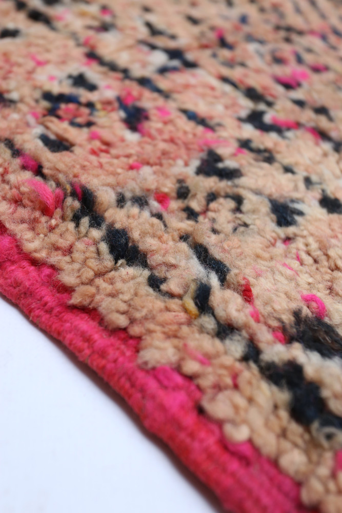 Tapis berbère aux tons beige et rose, orné de motifs noirs et colorés pour une touche artisanale et chaleureuse.