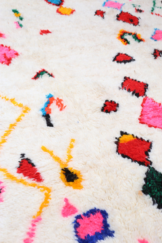 Tapis berbère à motifs géométriques colorés sur fond crème, dominé par des teintes roses, rouges, et bleues.