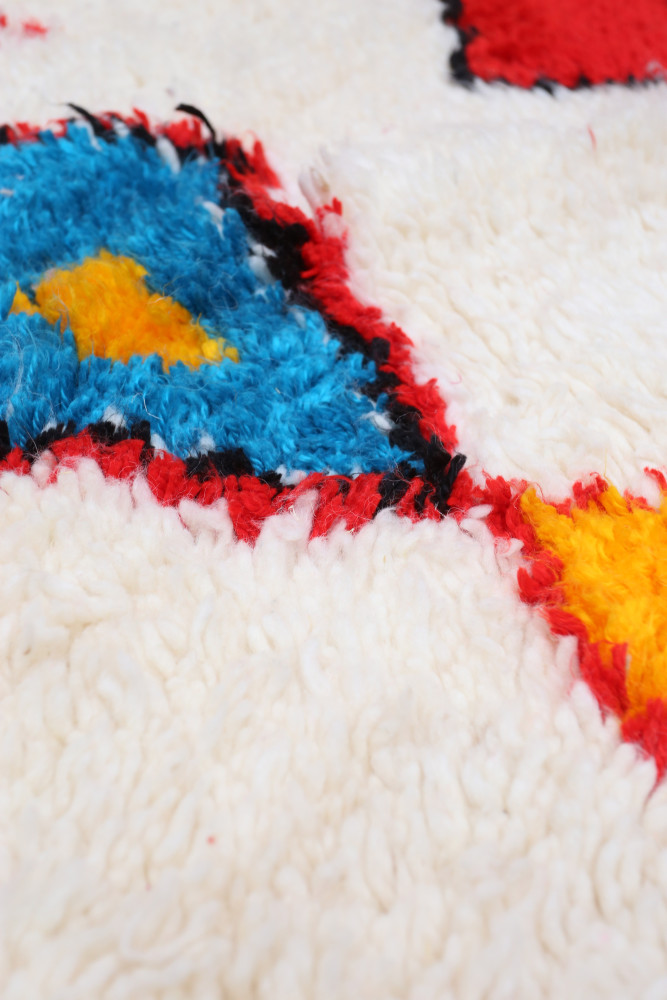 Tapis berbère aux motifs géométriques colorés, avec des teintes vives de bleu, rouge, jaune et blanc.