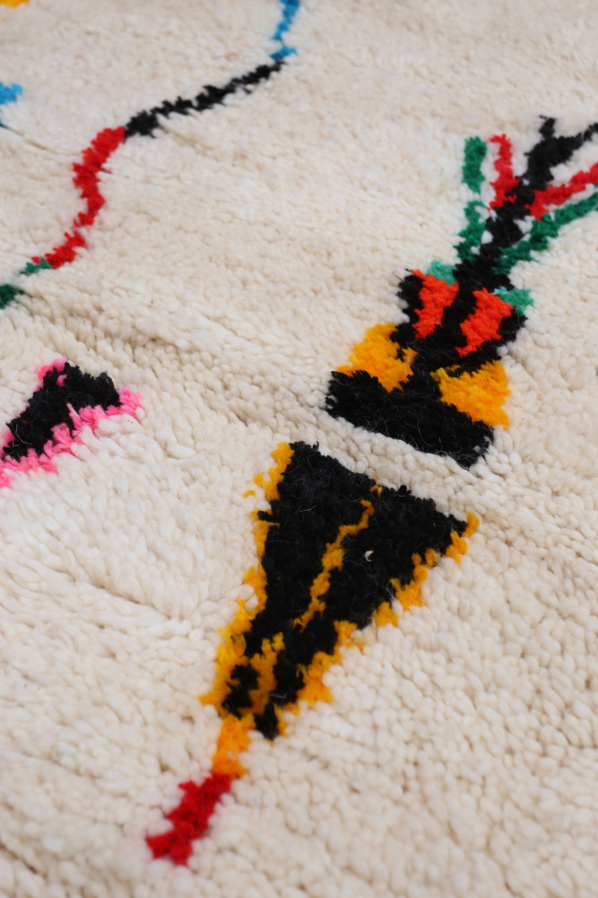 Tapis berbère aux motifs géométriques colorés, avec des tons de blanc, noir, rouge et jaune.