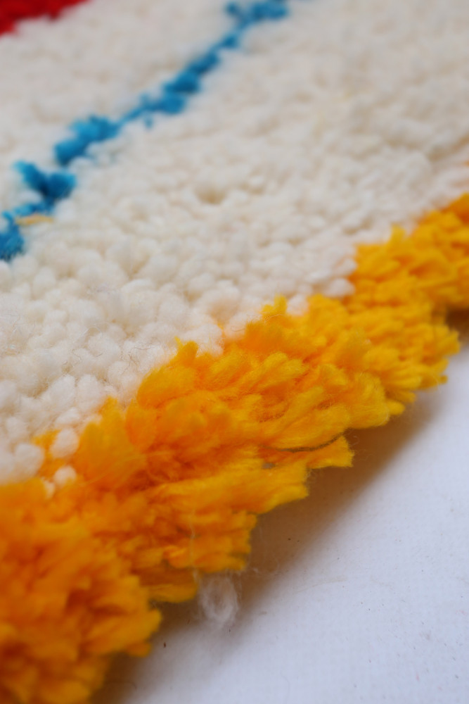 Tapis berbère au motif géométrique coloré avec des teintes vives de blanc, bleu et orange.