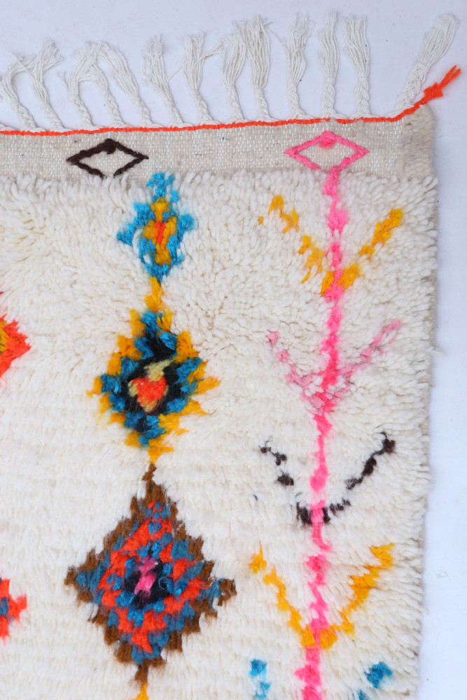 Tapis berbère en laine à motifs géométriques colorés, dominé par des tons crème, bleu, orange et rose.